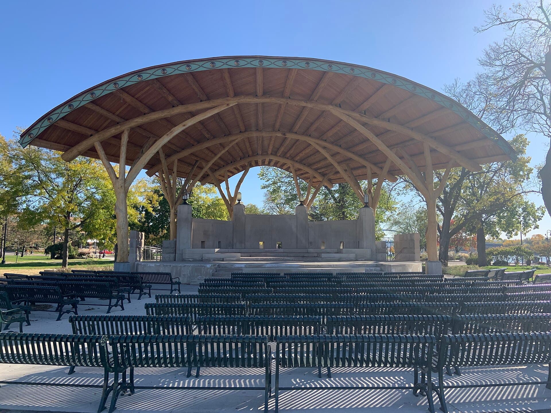 Empty seating in front of Riverside Park's wooden bandshell beneath a clear sky